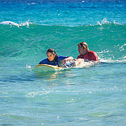 First take-off with help from your surf coach Your surf coach gives you a small push into the right wave – perfect timing for your first take-off during the beginner surf lesson.