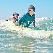 Surf instructor chooses the right wave and gives the board a push